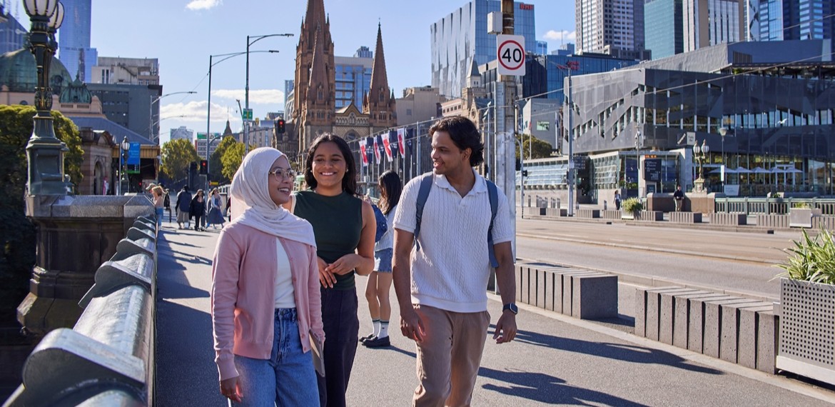 2 female and one male students walking along a bridge from flinders street station